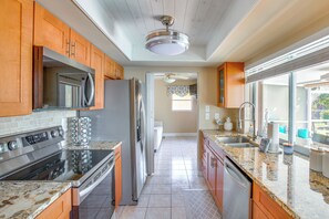 A modern kitchen with stainless steel appliances, wooden cabinets, granite countertops, and a view to the backyard. - Dock Your Boat: Waterfront Cape Coral Home w/ Pool (Cape Coral)
