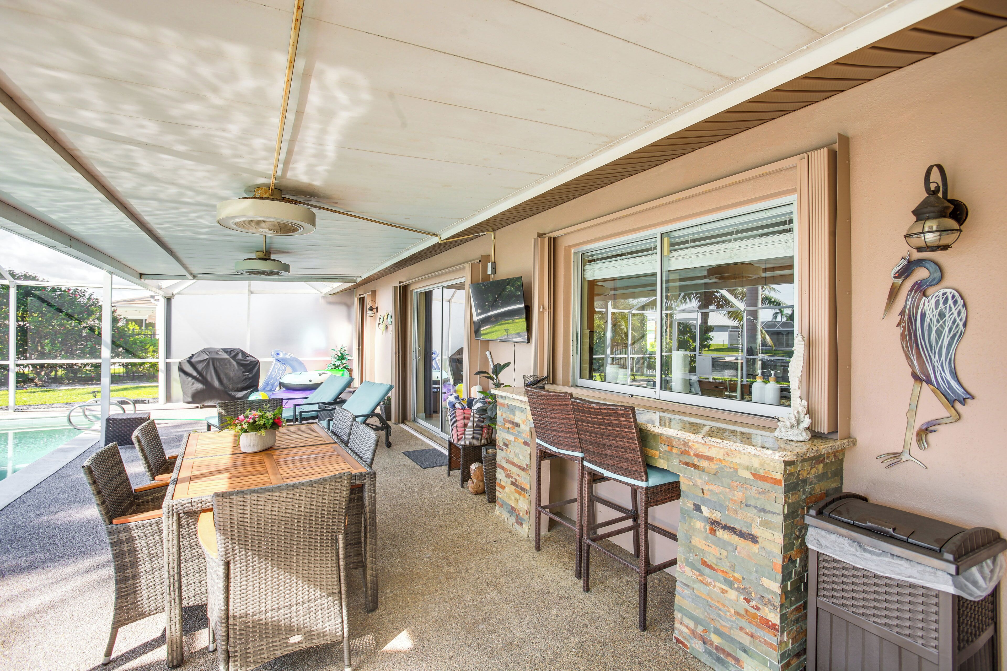 An outdoor patio with a wooden table and wicker chairs, a barbecue grill, and a stone fireplace.