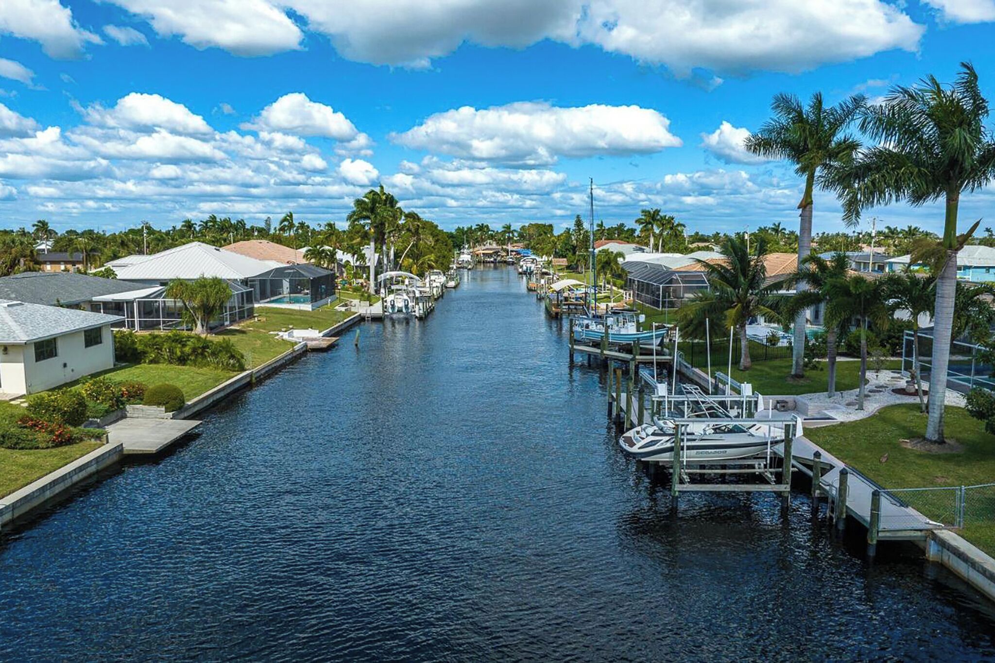 A canal lined with houses and boats, with palm trees and a clear sky.