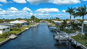 A canal lined with houses and boats, with palm trees and a clear sky. - Dock Your Boat: Waterfront Cape Coral Home w/ Pool (Cape Coral)