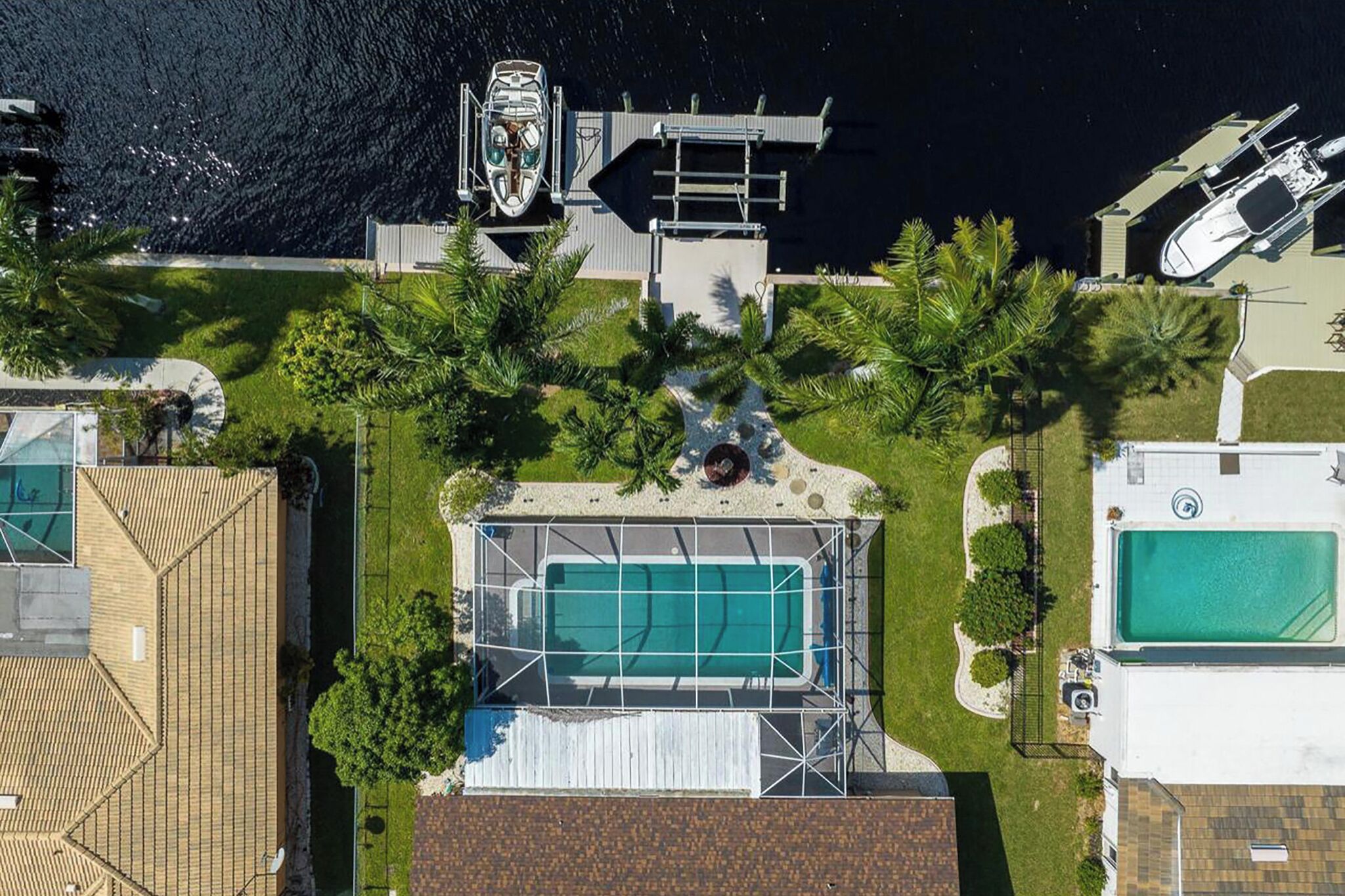 An aerial view of a property with a swimming pool, a dock with boats, and a well-maintained lawn.