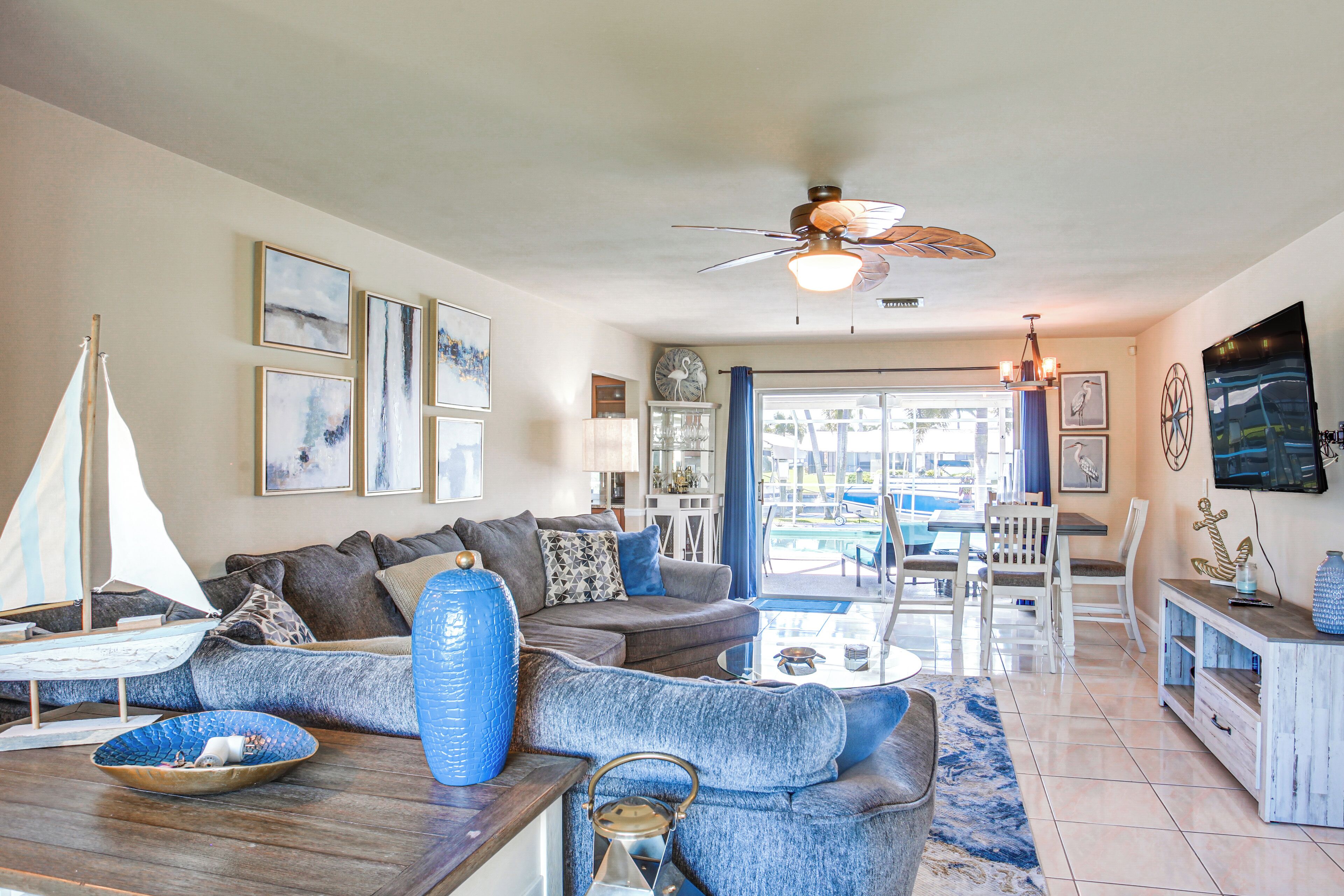 A spacious living room with a large sofa, a coffee table, and a sailboat model. There is a ceiling fan and a TV mounted on the wall.