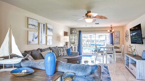 A spacious living room with a large sofa, a coffee table, and a sailboat model. There is a ceiling fan and a TV mounted on the wall. - Dock Your Boat: Waterfront Cape Coral Home w/ Pool (Cape Coral)