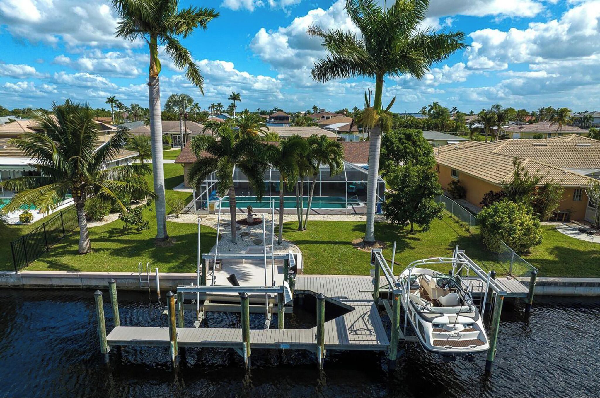A dock with a boat, a swimming pool, and palm trees in a residential area.