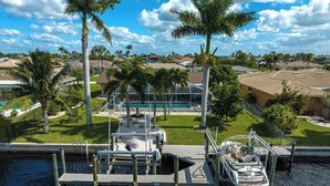 A dock with a boat, a swimming pool, and palm trees in a residential area. - Dock Your Boat: Waterfront Cape Coral Home w/ Pool (Cape Coral)