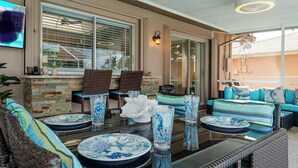 A sunlit patio area with wicker furniture, a stone fireplace, and a TV mounted on the wall. - Dock Your Boat: Waterfront Cape Coral Home w/ Pool (Cape Coral)