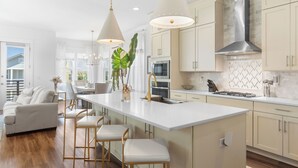 A modern kitchen with a central island, pendant lighting, and a large window. - Beachside Haven w/ Firepit, BBQ & Pool Access | Driftwood Dreams by AvantStay (Inlet Beach)
