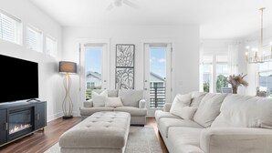 A spacious living room with a large flat-screen TV, a fireplace, and a modern chandelier. - Beachside Haven w/ Firepit, BBQ & Pool Access | Driftwood Dreams by AvantStay (Inlet Beach)