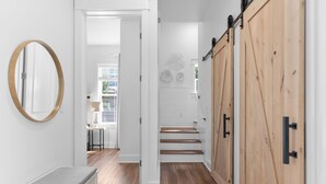 A hallway with wooden flooring, a white bench, and a wooden door with black handles. - Beachside Haven w/ Firepit, BBQ & Pool Access | Driftwood Dreams by AvantStay (Inlet Beach)