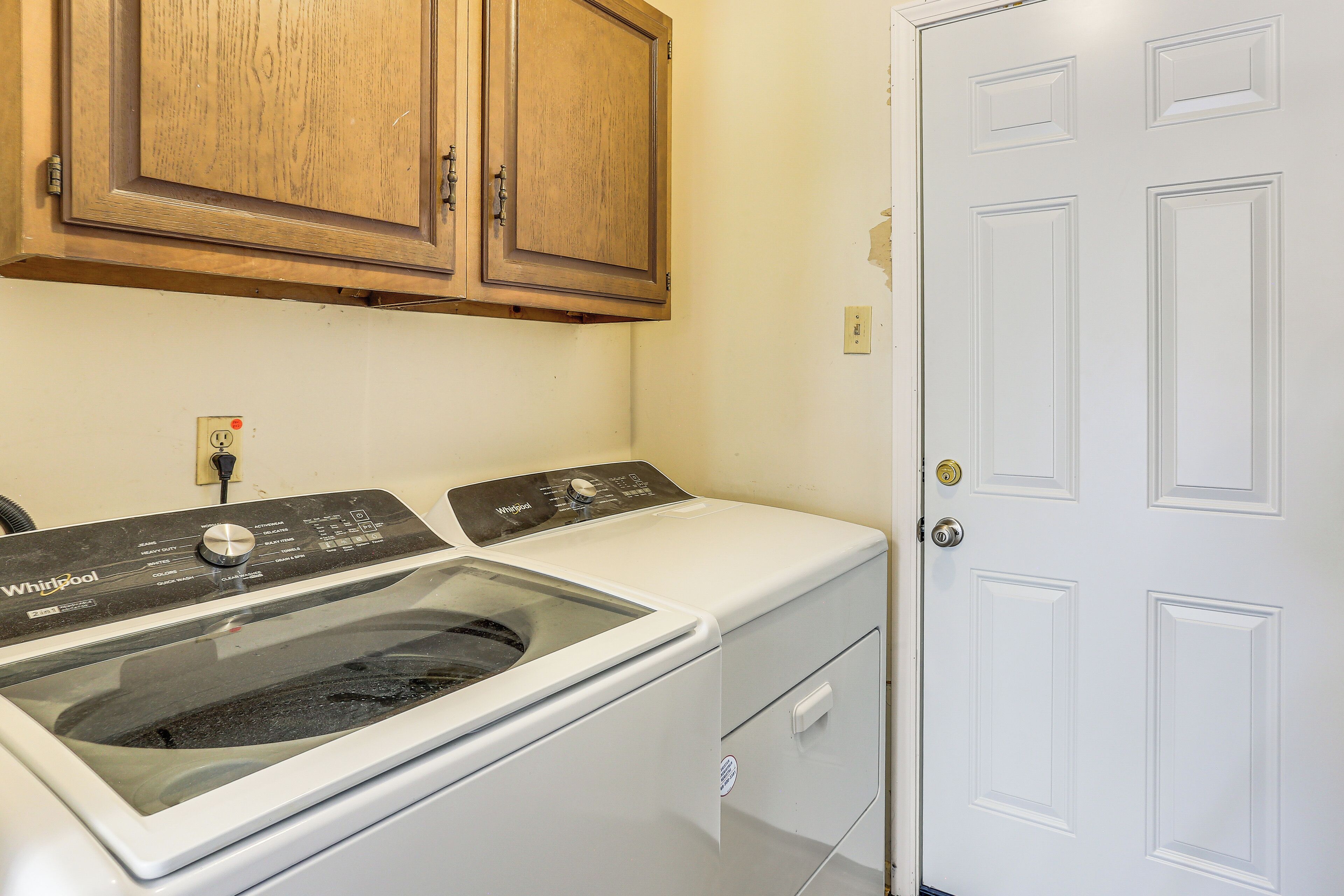 A laundry room with a Whirlpool washer and dryer, wooden cabinets, and a white door.