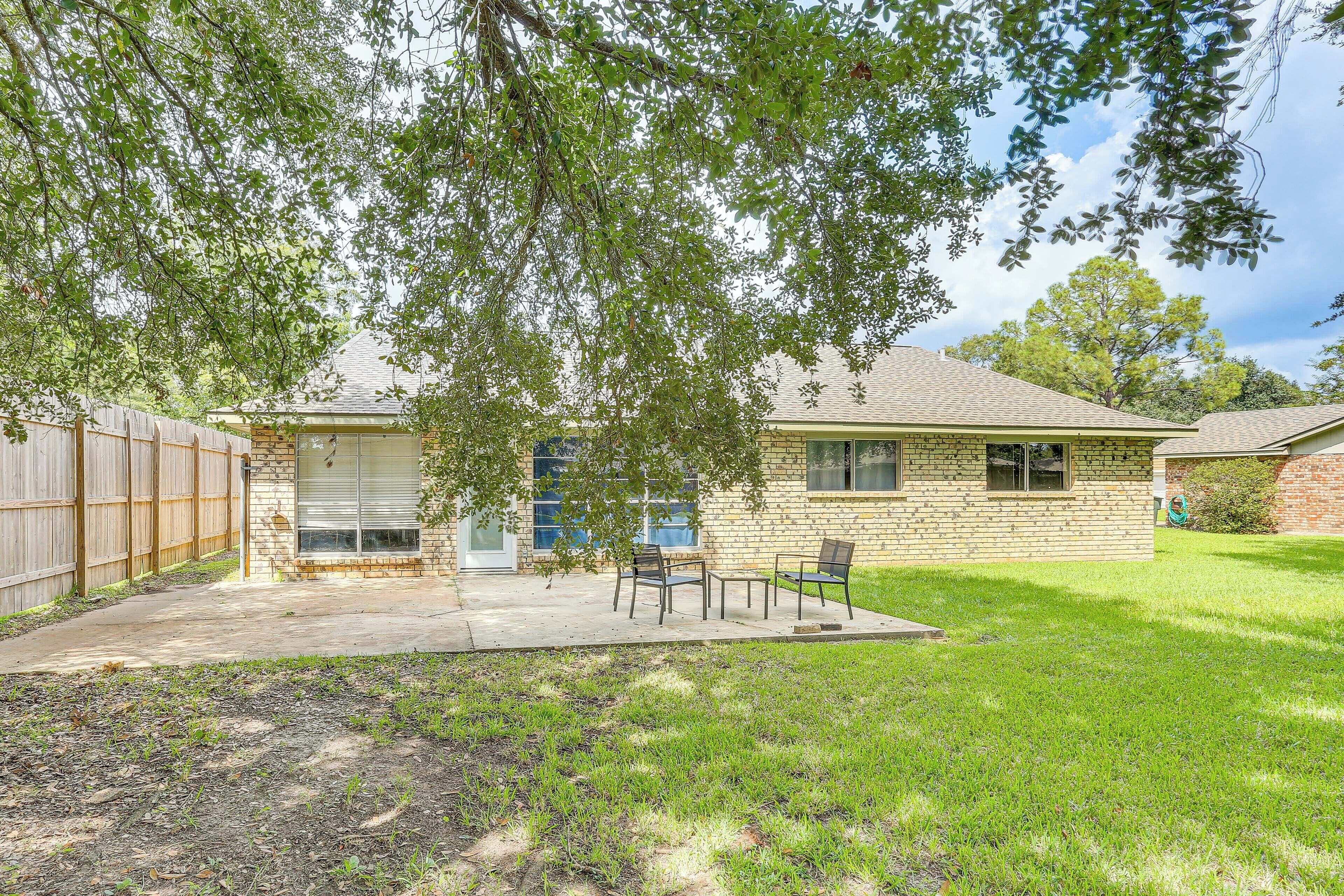 A house with a brick exterior, a covered patio with chairs, and a fenced backyard.