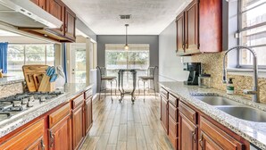 A kitchen with wooden cabinets, granite countertops, a gas stove, and a dining area with two chairs. - Fish, Golf, Explore: Home 3 Mi to Prien Lake Park! (Lake Charles)