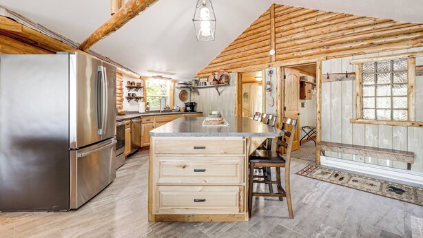 A modern kitchen with wooden beams, stainless steel appliances, and a large island with drawers. - Water's Edge Retreat on Butternut Lake! (Butternut)