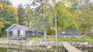 A lakeside cabin with a dock, surrounded by trees and a stone wall. - Water's Edge Retreat on Butternut Lake! (Butternut)