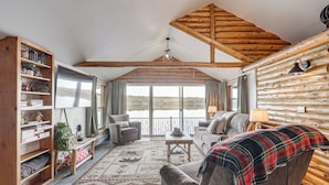 A cozy log cabin interior with a large window, wooden furniture, and a view of the outdoors. - Water's Edge Retreat on Butternut Lake! (Butternut)