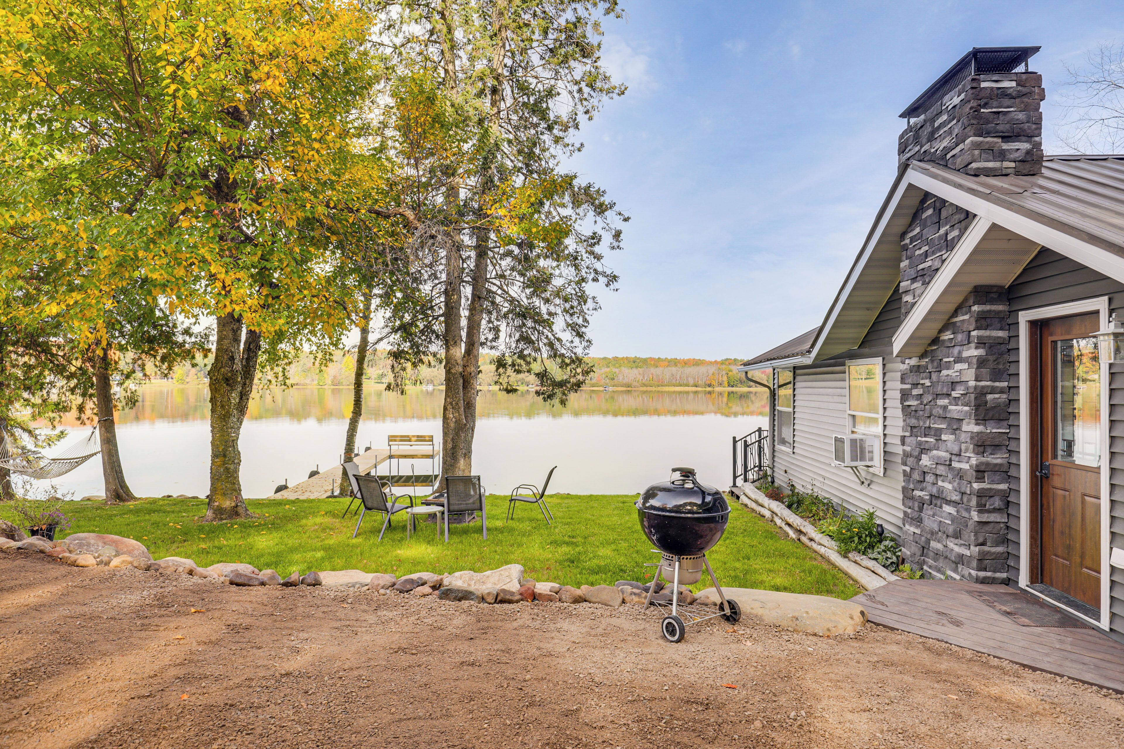 A lakeside cabin with a stone exterior, a deck, and a grill.