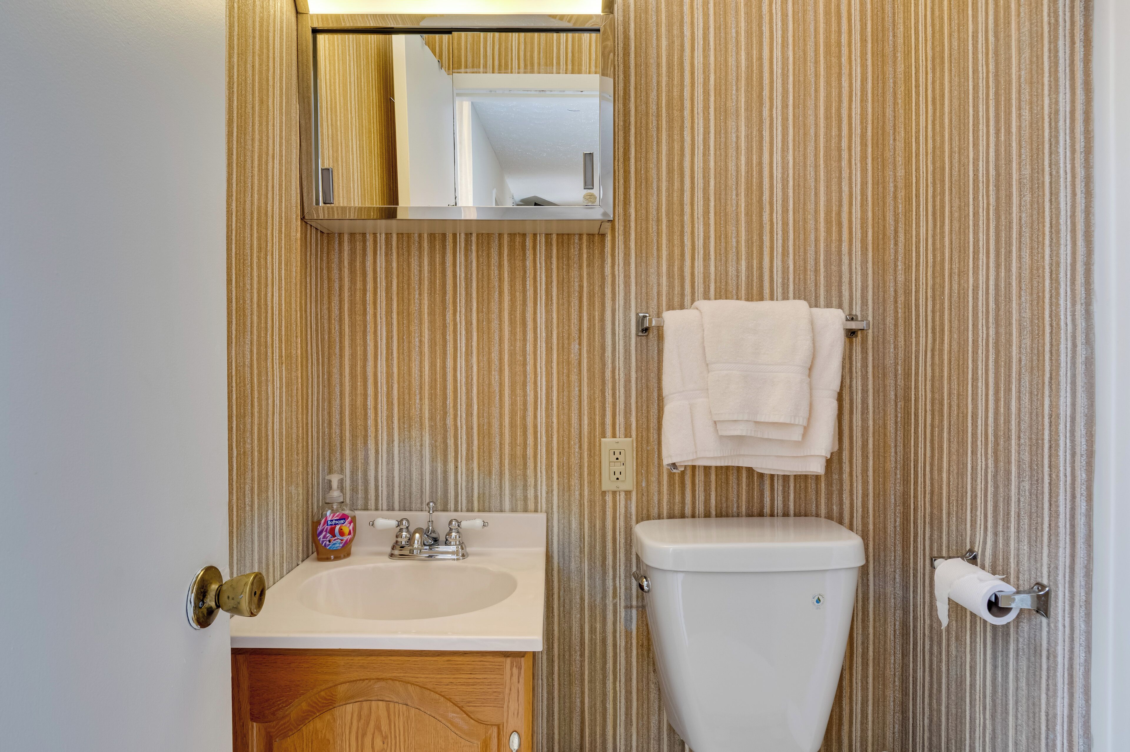 Un baño con tocador de madera, lavamanos, inodoro, toallero y espejo.