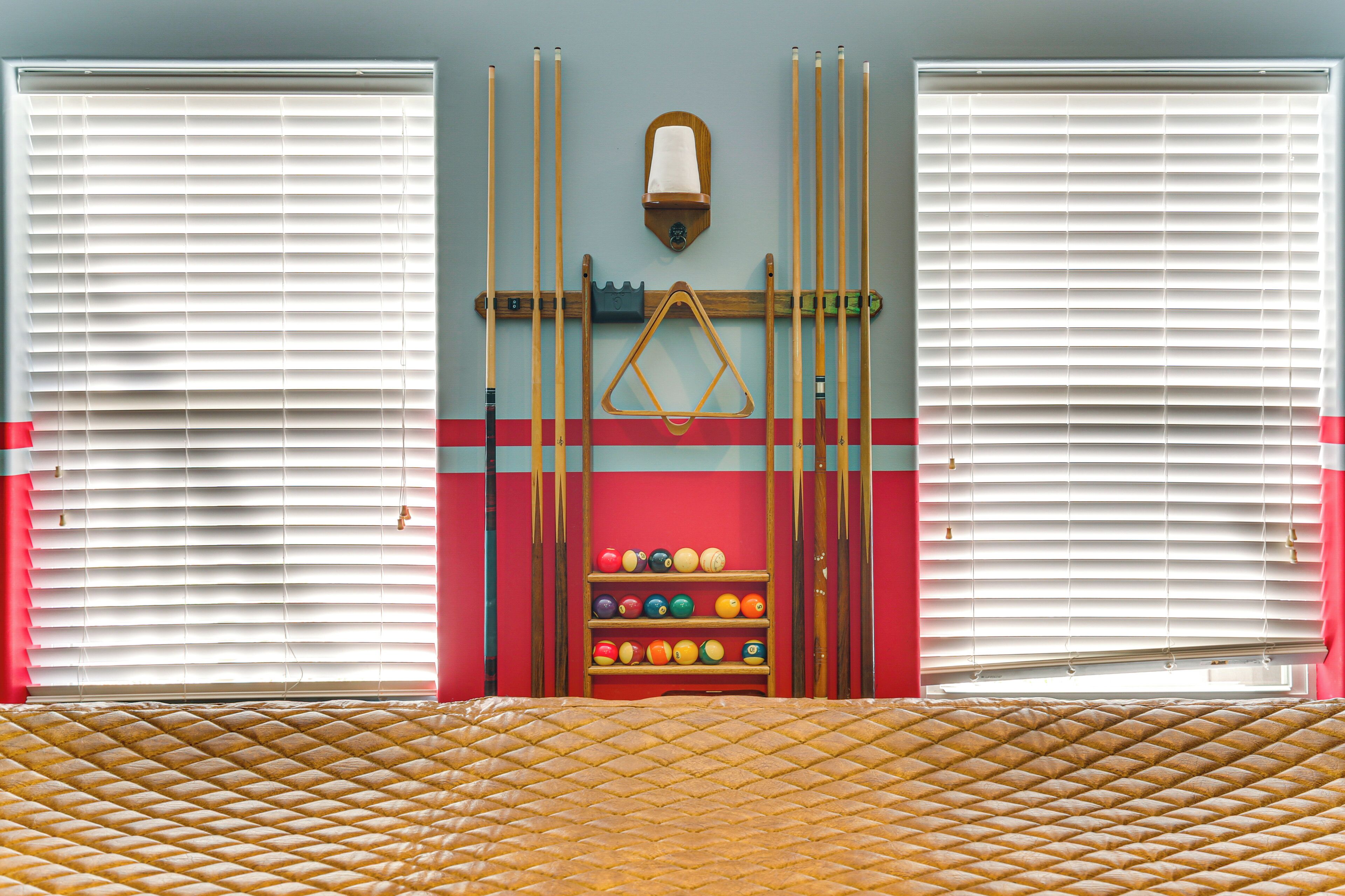 A room with a billiards setup, including a rack, cue sticks, and a ball rack.