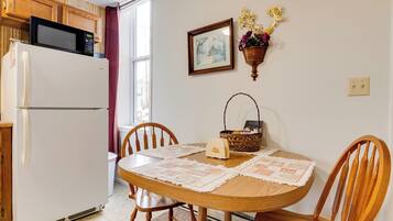 A kitchen with a white refrigerator, wooden cabinets, a microwave, a dining table with placemats, chairs, a basket, and a wall-mounted flower pot.