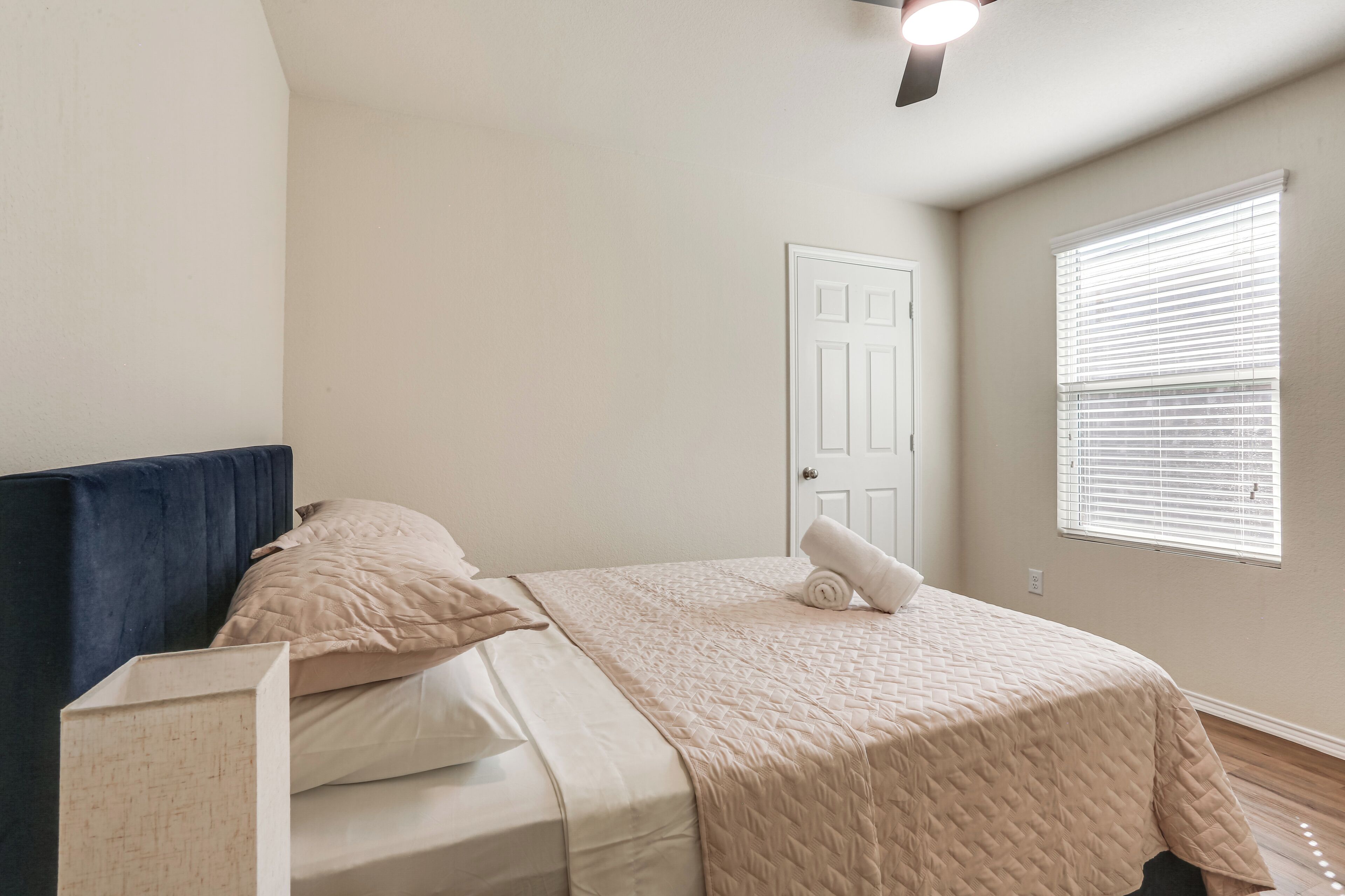 A bedroom with a bed, a ceiling fan, a door, and a window with blinds.