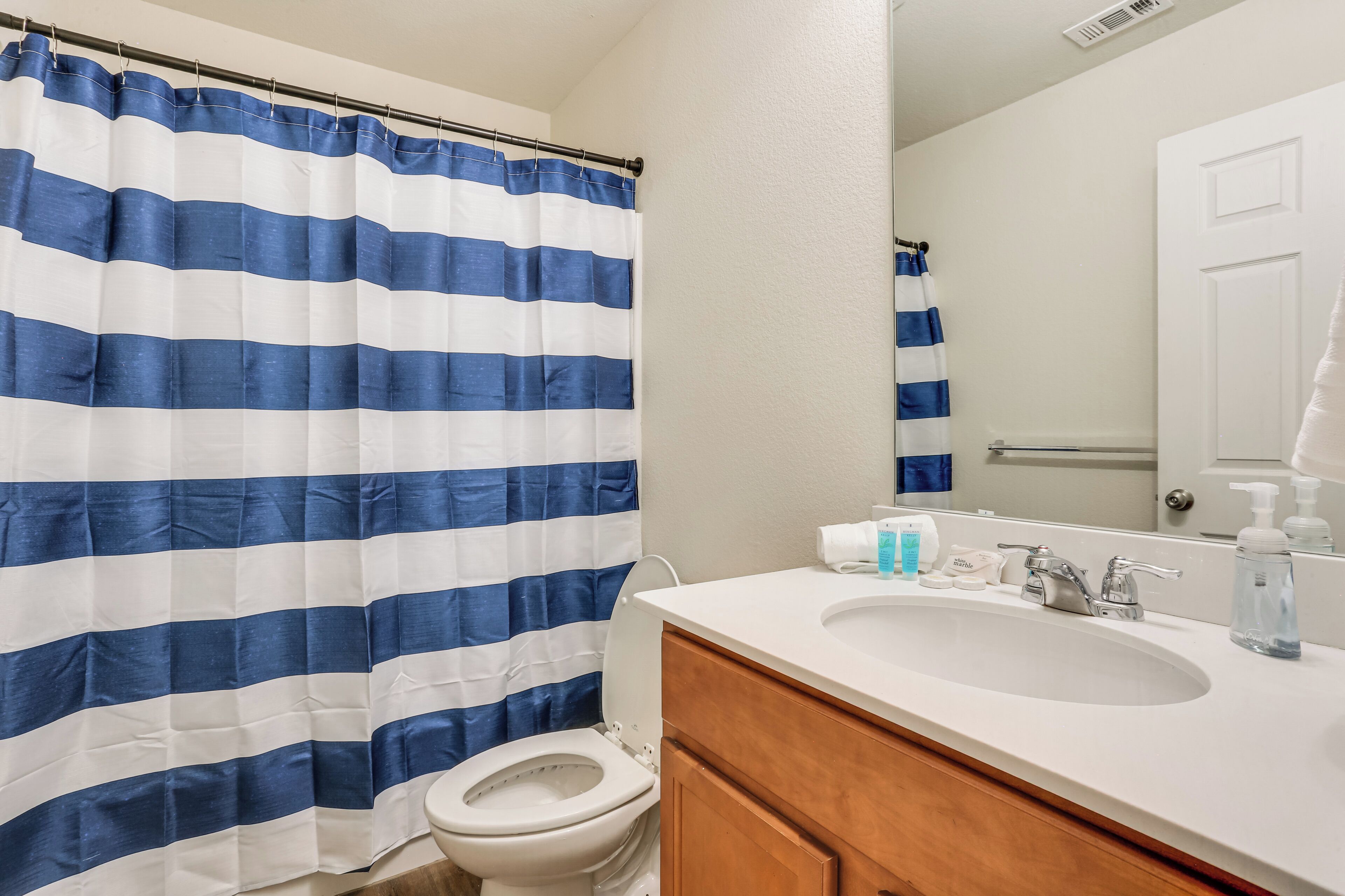 A bathroom with a striped shower curtain, a toilet, a sink with toiletries, and a mirror.