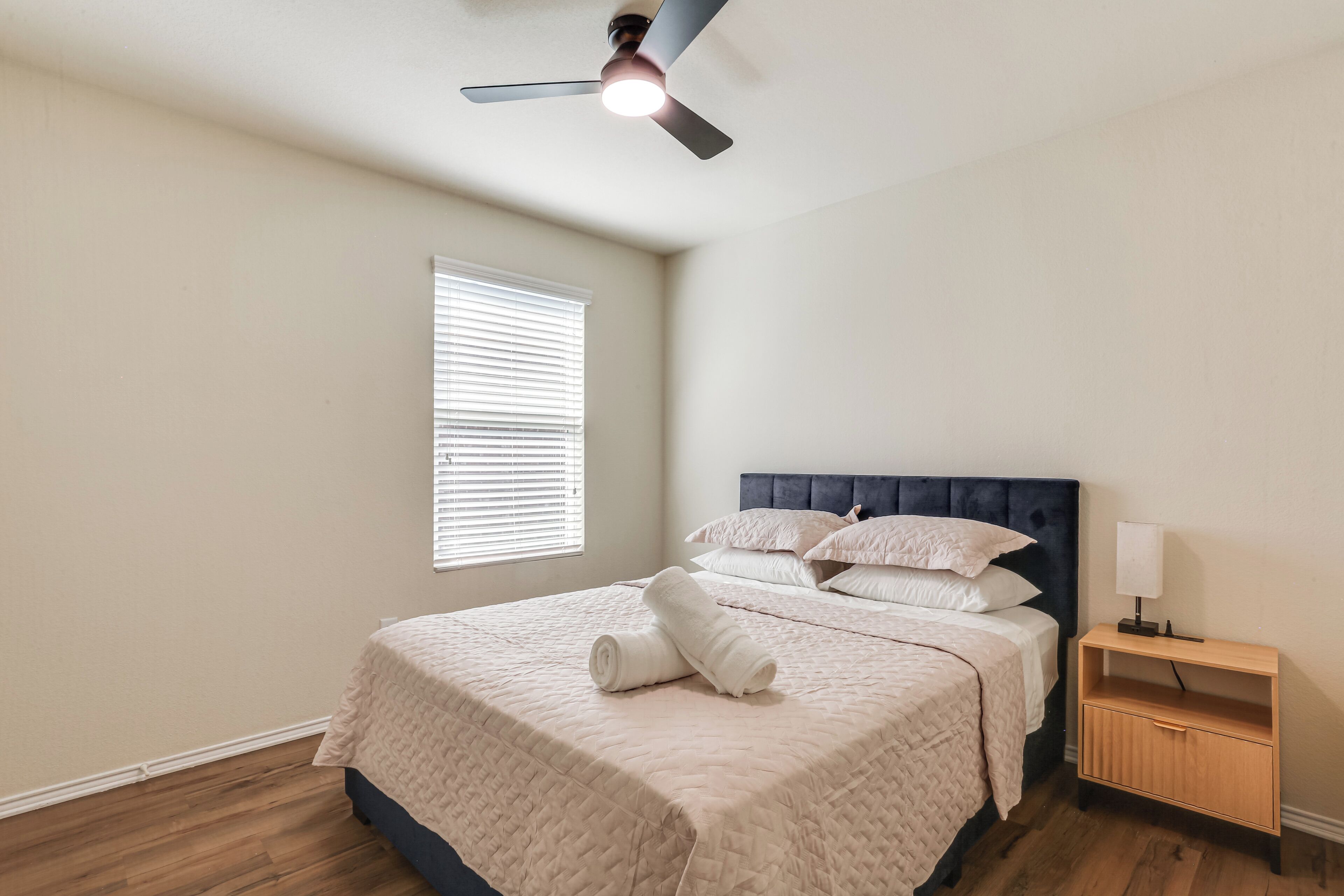 Ein Schlafzimmer mit Bett, Nachttisch, Deckenventilator und Fenster.