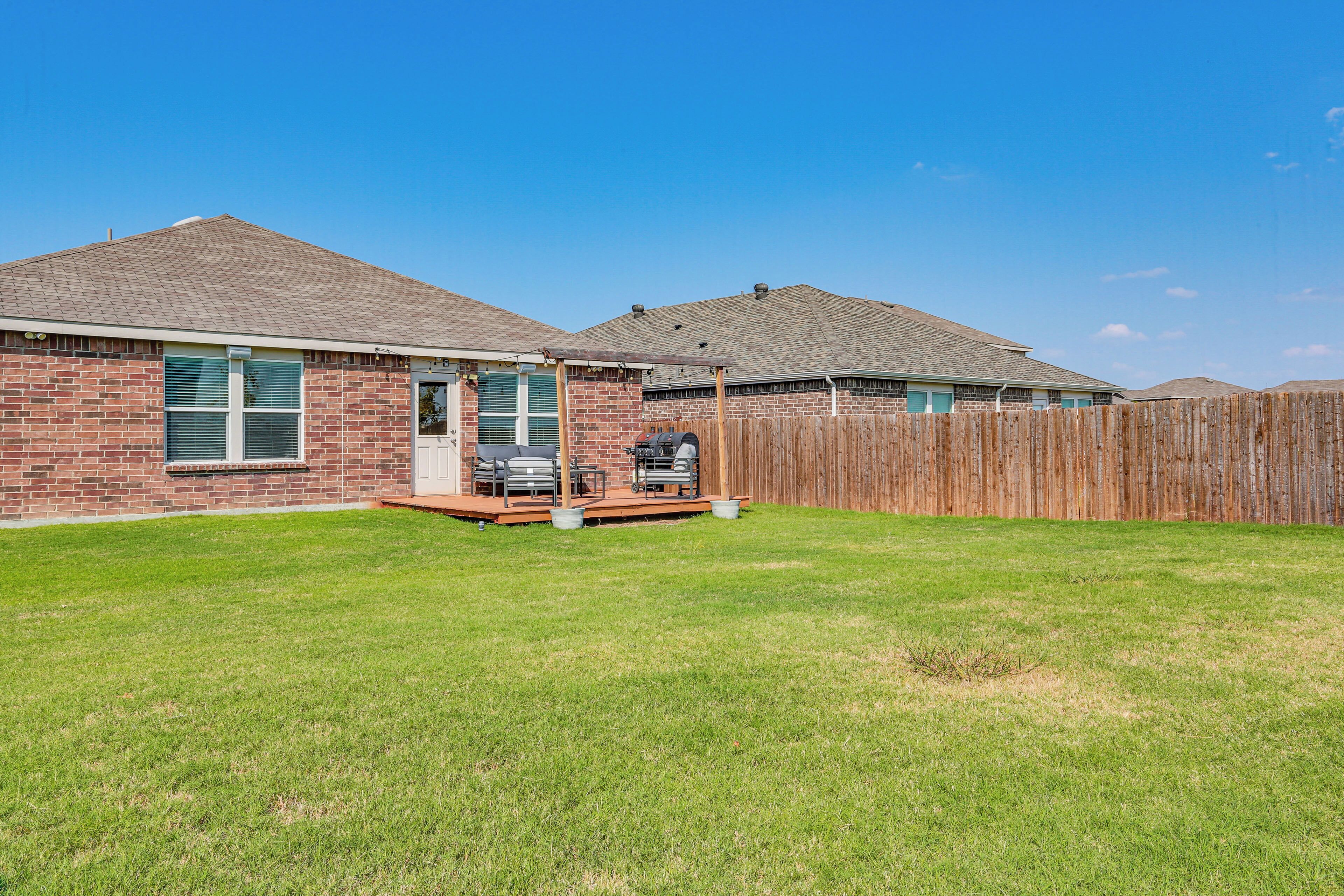 A residential backyard with a brick house, a wooden deck, and a fenced area.