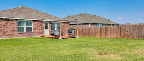 A residential backyard with a brick house, a wooden deck, and a fenced area.