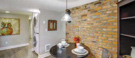 A dining area with a brick wall, a round table with chairs, and a hanging light fixture.