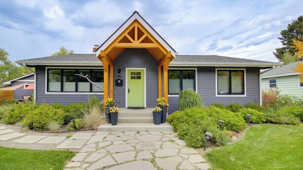 Une maison moderne avec une façade grise, une porte verte et un chemin de pierre menant à l’entrée.