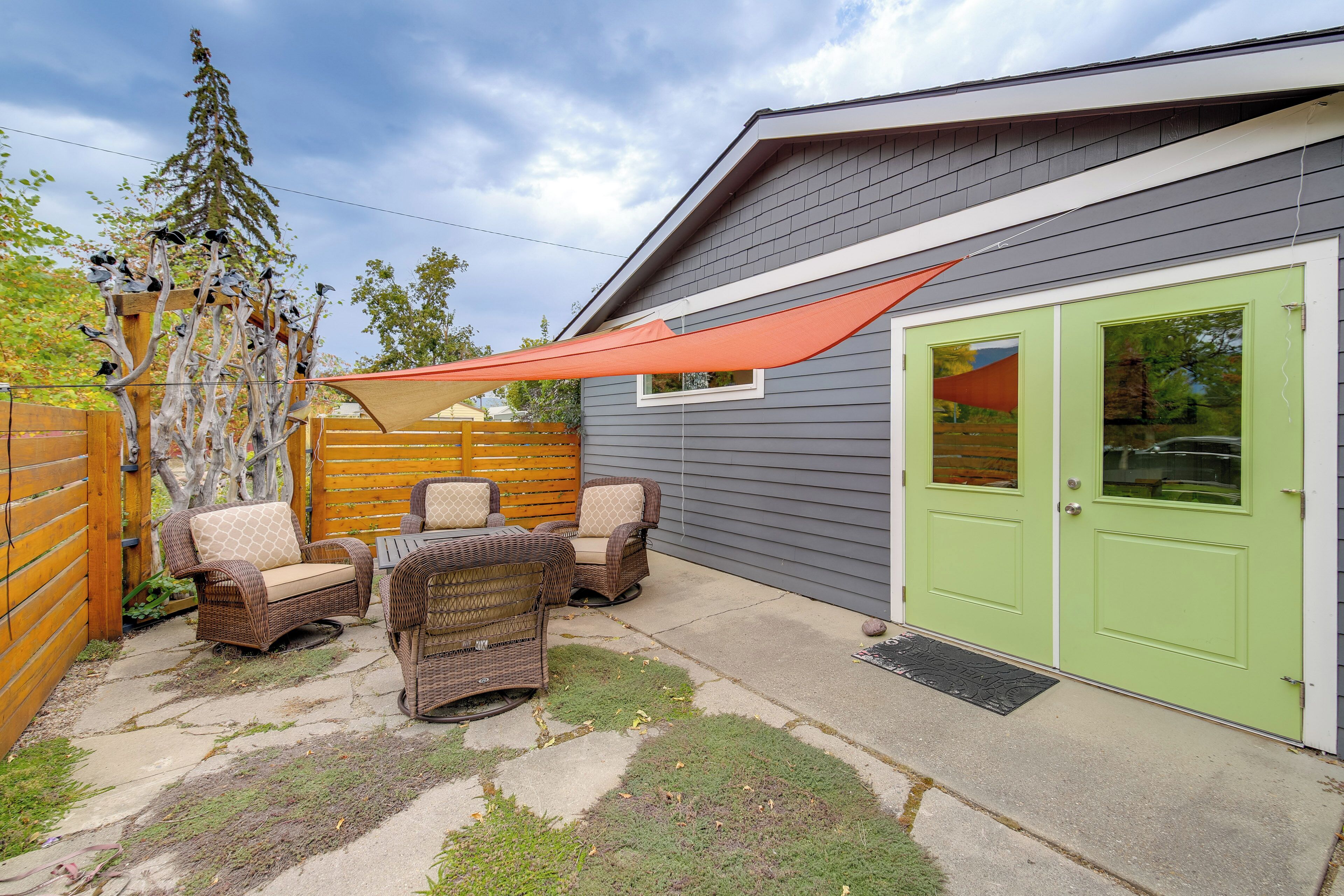 Une terrasse avec des meubles en osier, une porte verte et une clôture en bois.