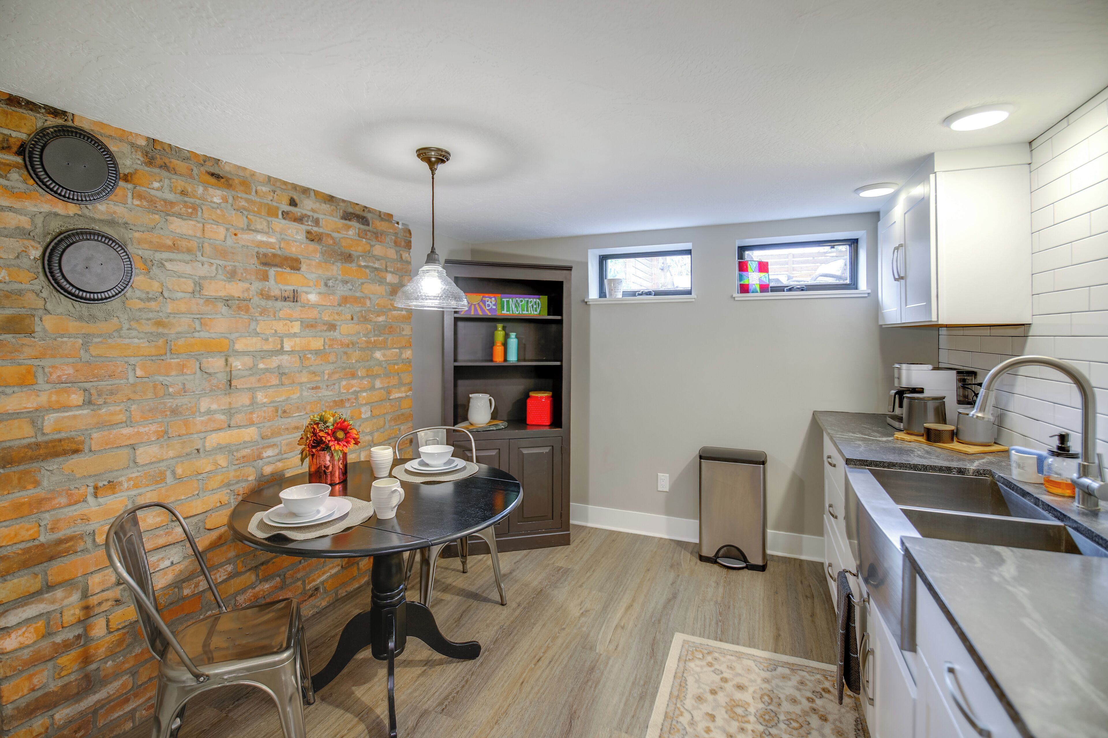Una cocina moderna con pared de ladrillo, comedor con mesa y sillas, y ventana con vistas.