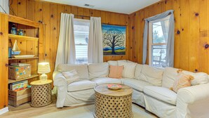 A cozy living room with a white sectional sofa, a wooden bookshelf, and a round coffee table. - Cozy Cottage Just 2 Blocks From the River! (Colonial Beach)