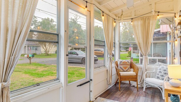 A cozy room with large windows, wicker furniture, and a wooden table with a lamp. - Cozy Cottage Just 2 Blocks From the River! (Colonial Beach)