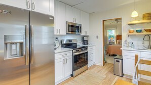 A modern kitchen with stainless steel appliances, white cabinetry, and a wooden dining table. - Cozy Cottage Just 2 Blocks From the River! (Colonial Beach)