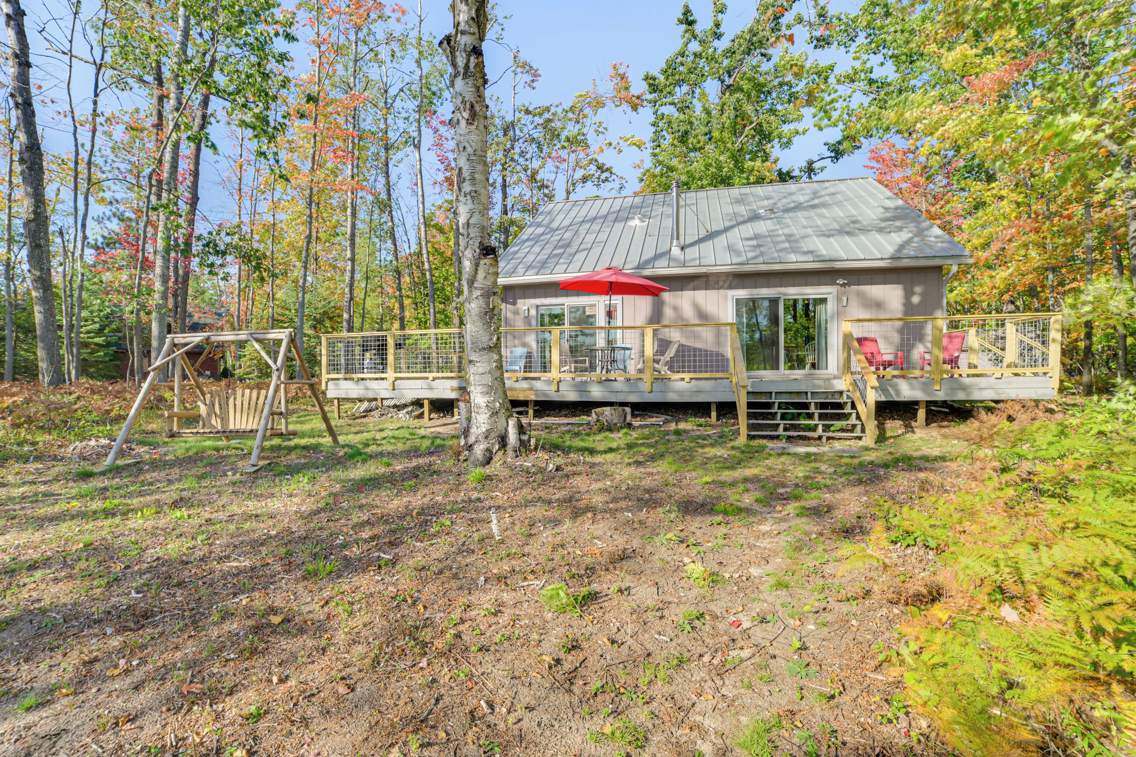 A cabin with a deck, a swing set, and a red umbrella.