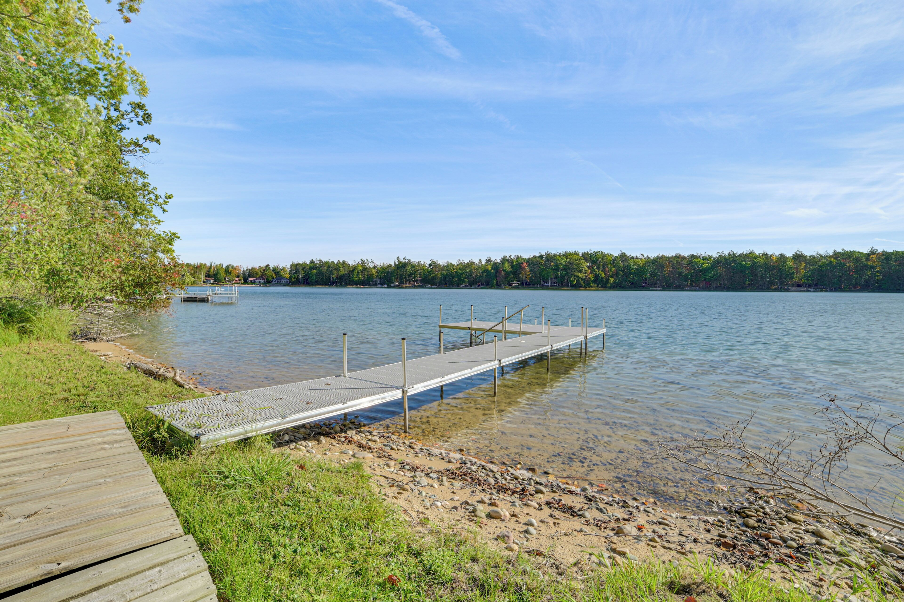 A wooden dock extending into a calm lake, surrounded by grassy areas and trees.