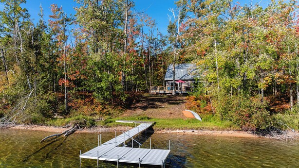 Une cabane entourée d’une forêt, avec une jetée qui s’avance sur un lac aux eaux limpides.
