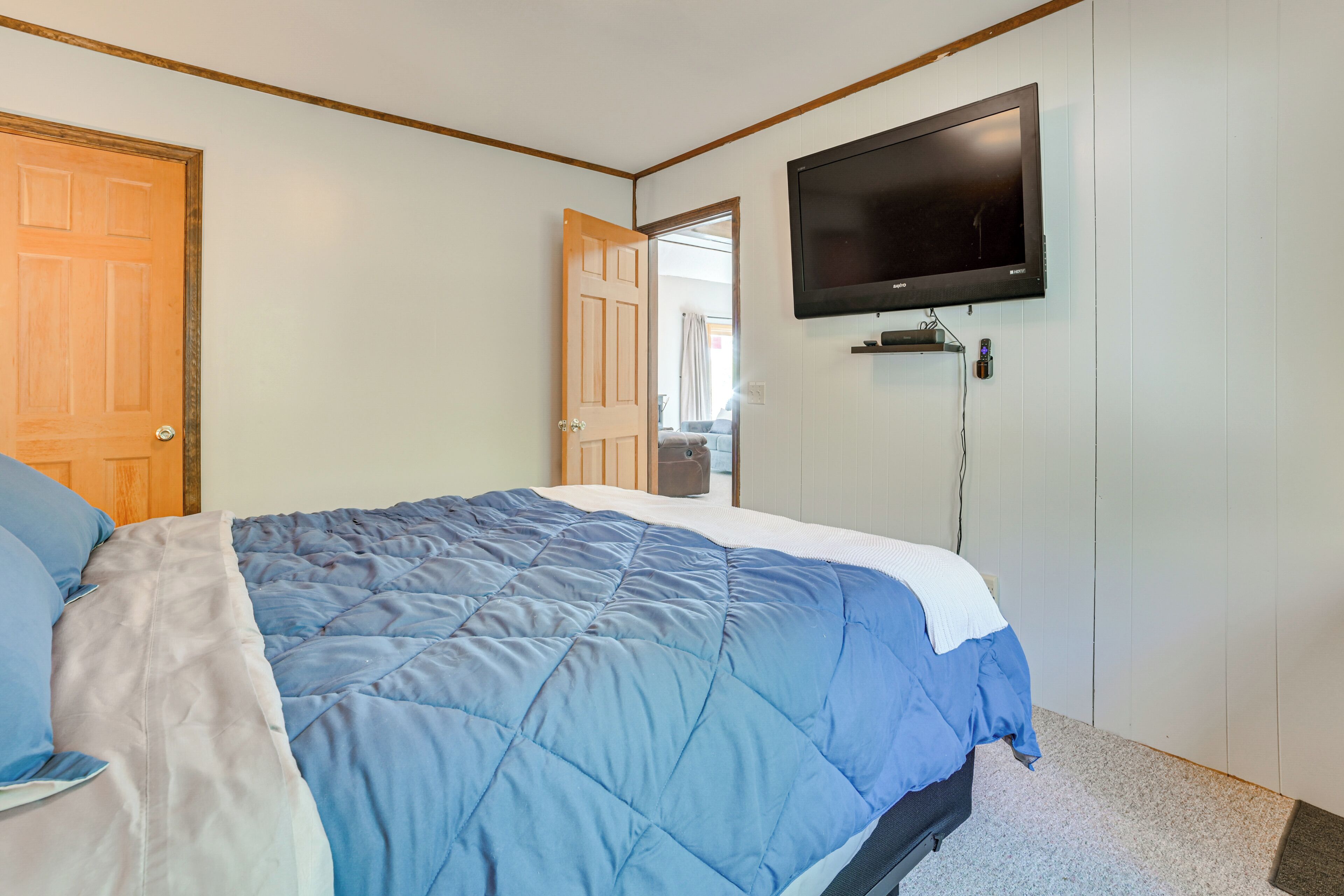 Een slaapkamer met een bed, een aan de muur bevestigde televisie en een deur die naar een andere kamer leidt.