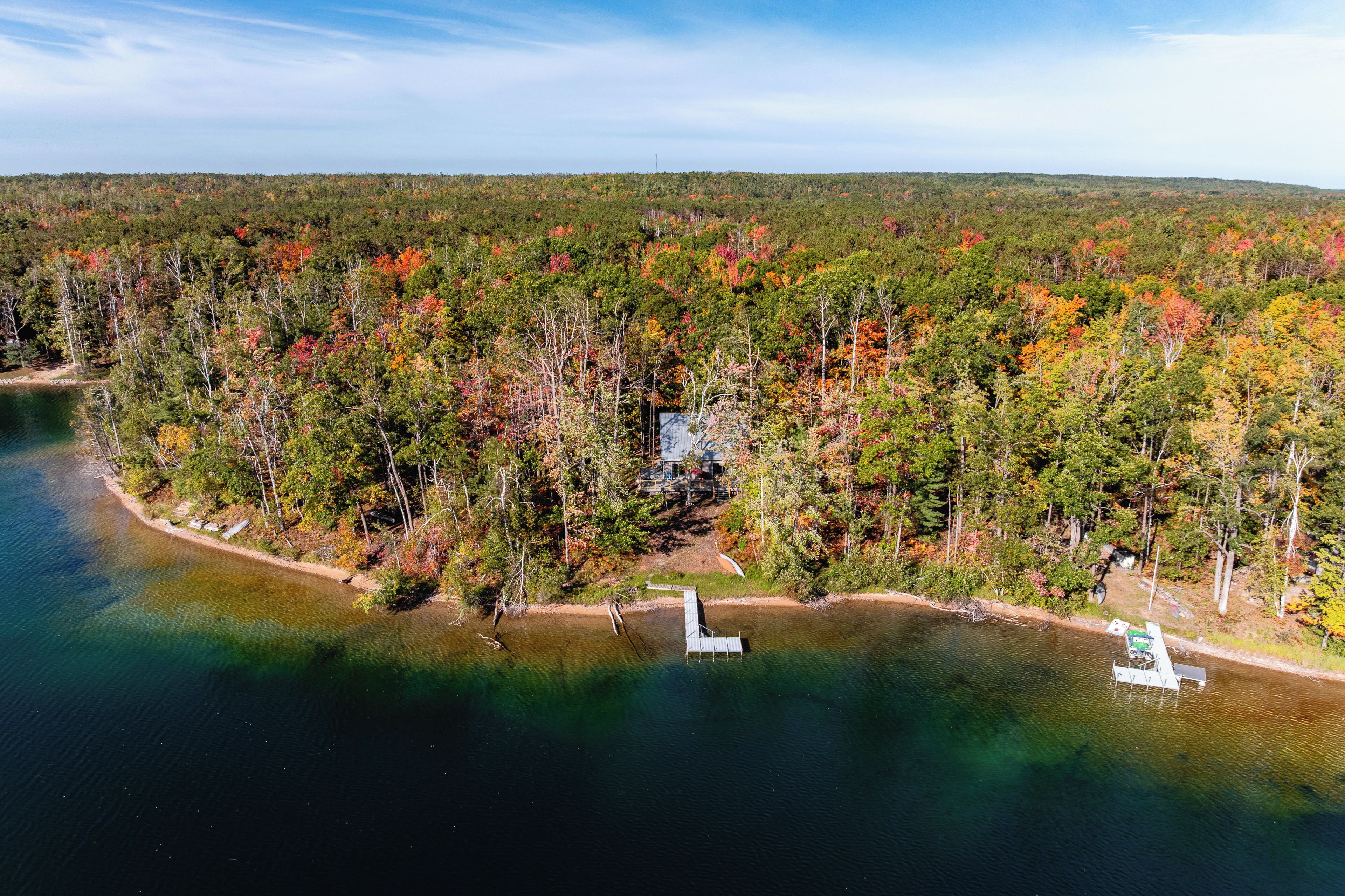 An aerial view of a lakeside property with a dock, surrounded by dense forest and a clear sky.
