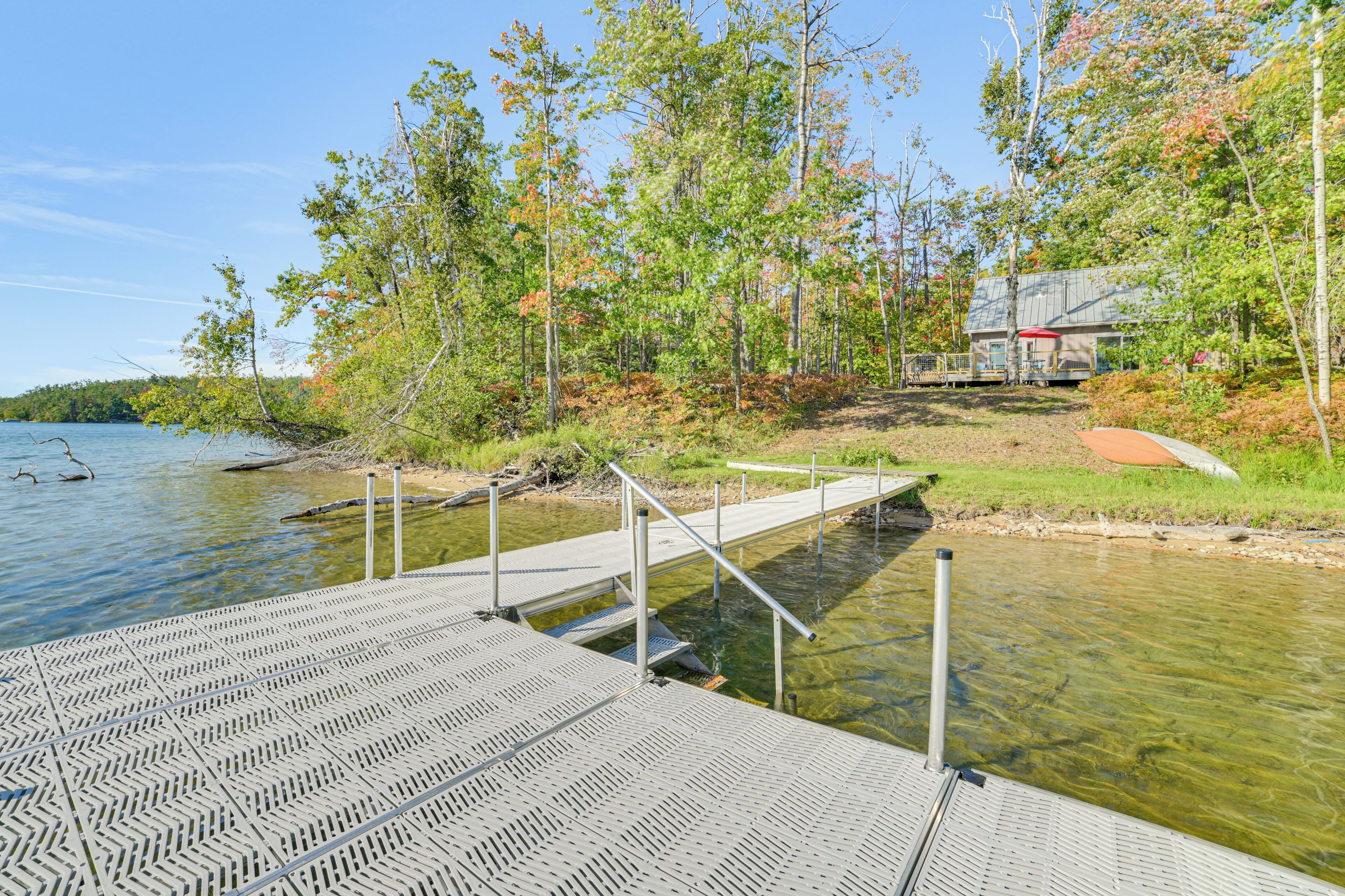 A wooden dock extending into a clear lake, surrounded by trees and a building in the background.