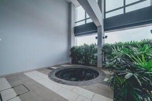 Un espacio interior moderno con una fuente circular, plantas en macetas y un amplio ventanal que proporciona luz natural.