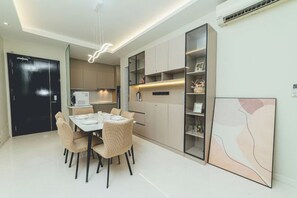 Una cocina moderna con zona de comedor, que incluye una mesa y sillas blancas, una puerta negra y un estante montado en la pared con adornos.