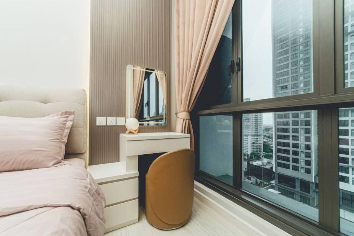 A bedroom with a bed, a bedside table, a mirror, a lamp, and a window with a city view.