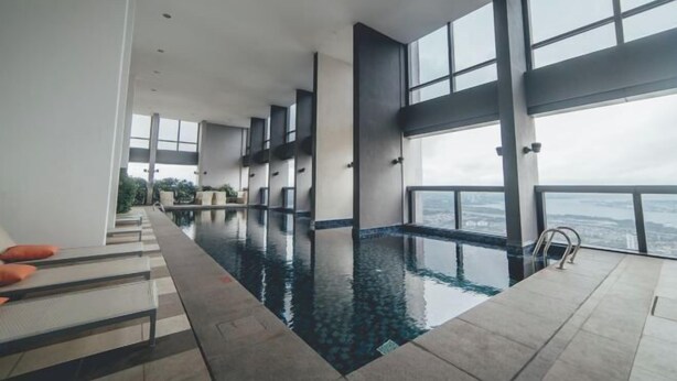 A modern indoor swimming pool with tiered seating and large windows offering a city view. - Sky88 Residence Johor Bahru (Johor Bahru)