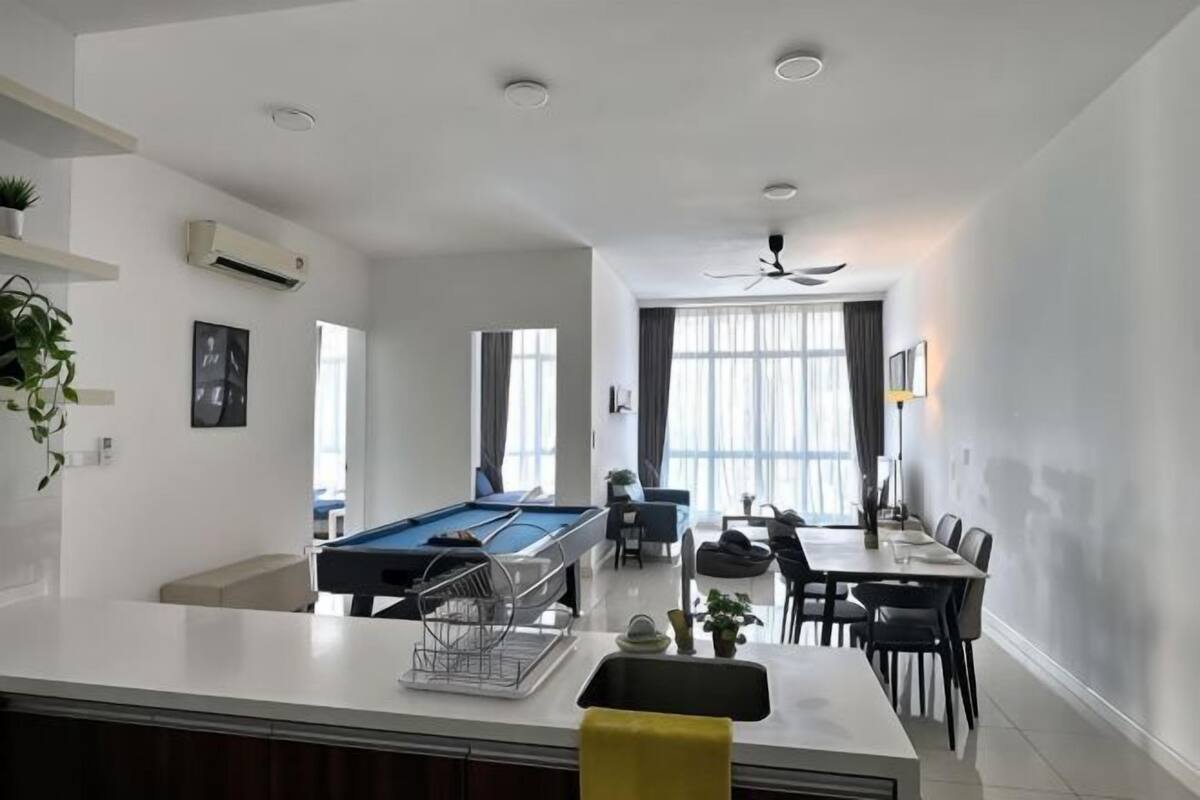 A modern living room with a pool table, dining area, and a kitchen counter.