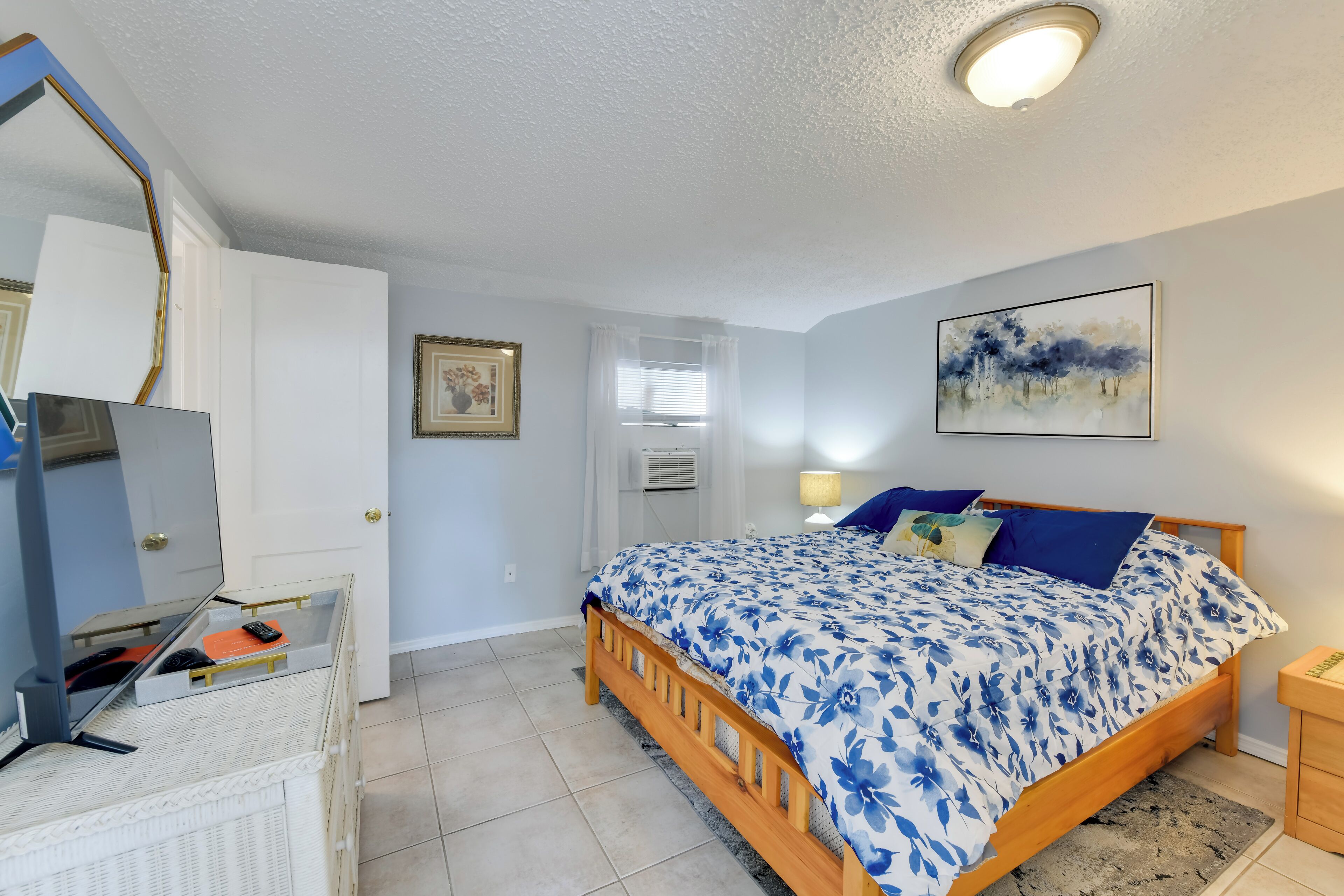 Un dormitorio con cama de madera, cómoda blanca, espejo y un cuadro en la pared.