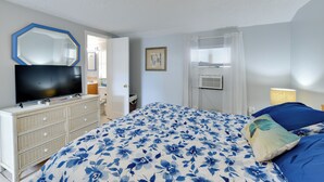 Ein Schlafzimmer mit Bett, Kommode, Fernseher und einer Tür zu einem anderen Raum.