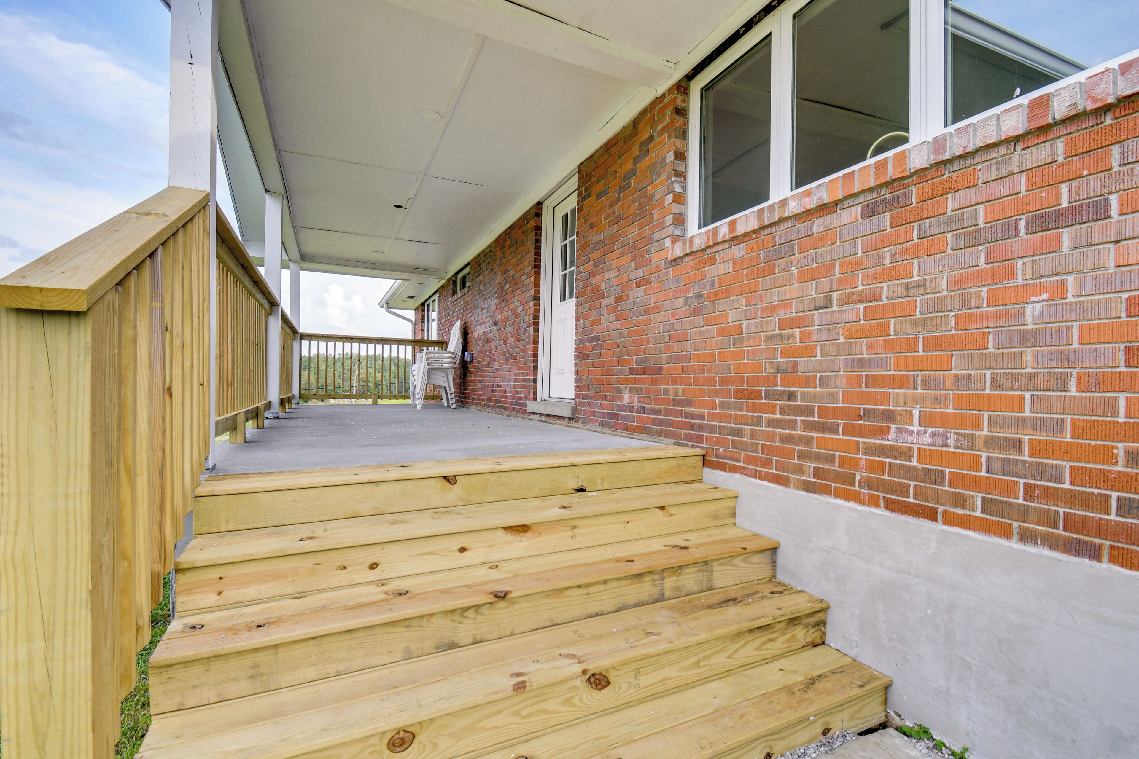 En træt trappe fører op til en overdækket veranda med murstensfacade.