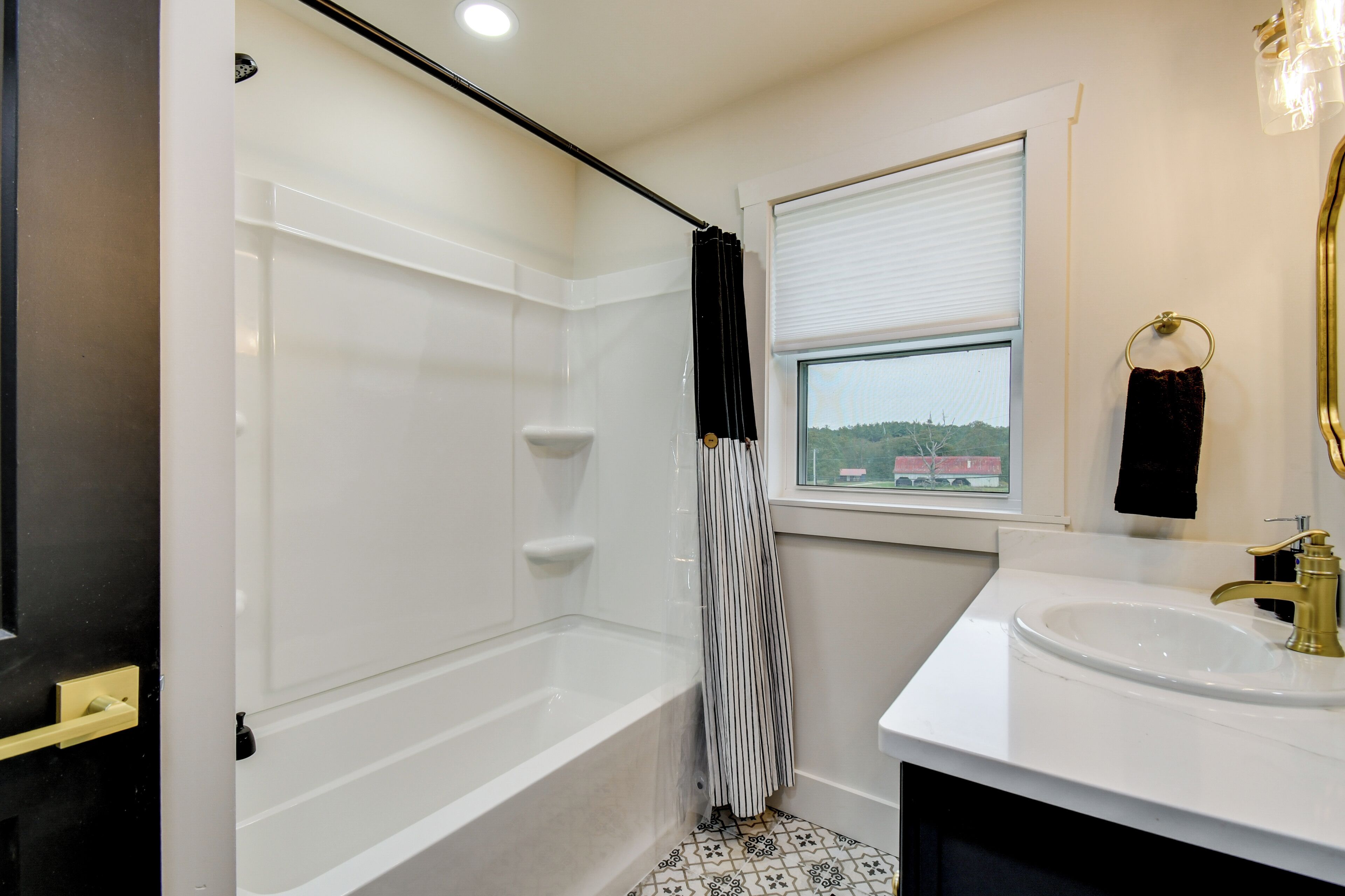 A bathroom with a bathtub, a window with a view, a sink with a gold faucet, and a towel ring.